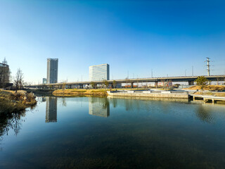 Naklejka premium Tranquil River View Reflecting Urban Architecture Under Clear Blue Skies