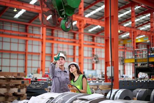 Two workers in safety gear inspect the industrial plant, pointing towards something in the factory