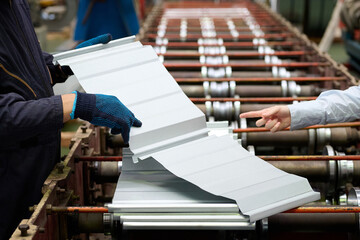 Workers in a factory are inspecting metal sheets on a production line, showcasing industrial...