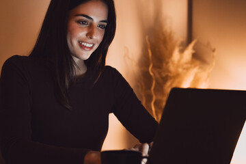 Head shot pleasant happy young woman freelancer working on computer at night. Attractive businesswoman studying online, using laptop software, web surfing information or shopping in internet store.