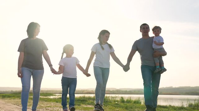 Family walk hand in hand along lake shore at sunset, parent and child hold hand, two child and parent linked together, nature grass and water, warm light and reflection, subtle love and together