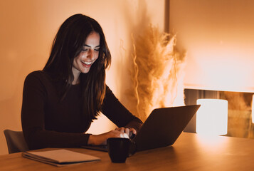 Head shot pleasant happy young woman freelancer working on computer at night. Attractive businesswoman studying online, using laptop software, web surfing information or shopping in internet store. © Daniel