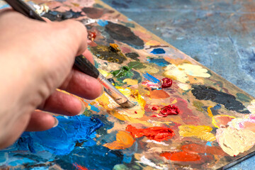 Artist's hands with old used brushes in an artist's studio, palette with multi-colored spots of oil or acrylic paint