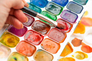 Artist's hand with brush. Watercolor paint in old used plastic palettes, creative mess