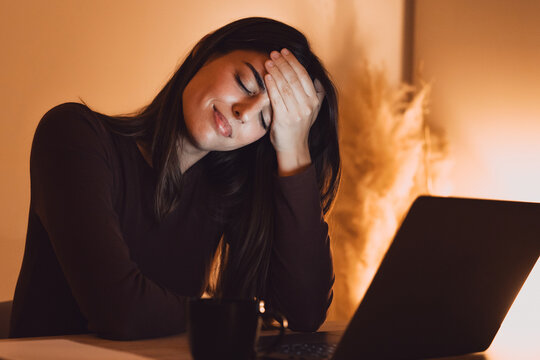 Tired woman massaging temples, suffering from headache after computer work, sitting at desk with laptop at home, exhausted young female with closed eyes touching head, relieving pain, migraine - Powered by Adobe