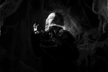 Screaming creepy woman covered with spiderweb on black background. Black and white photo. Halloween...