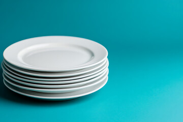 Minimalist stack of white plates against a teal backdrop. The simplicity and clean lines create a modern and elegant look, perfect for showcasing tableware design.