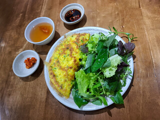 Traditional Vietnamese crispy pancake banh xeo served in a vegetarian version with a variety of fresh herbs and lettuce. On the side are dipping sauces including soy with chili, fish sauce-style