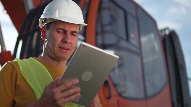 Inspecting construction site with tablet worker in hard hat safety vest reviews plan on tablet near excavator while engineer checks operation and technology supports inspection with focused face