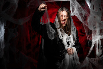 Obraz premium gothic woman with creepy vampire makeup trapped in spider web trying to scare showing strike gesture and fist-up. Fantasy scary girl on red halloween background.