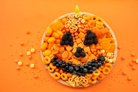 Halloween Jack O Lantern board, fun orange and black food mix. Party spooky salty snacks and fruits