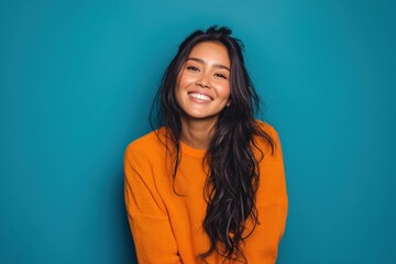 Fototapeta premium Smiling person with long dark hair wearing an orange sweater, looking cheerful. The vibrant image captures warmth and joy. The scene is bright and uplifting, creating a positive vibe