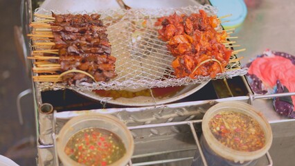 Grilled meat skewers arranged with sauces on stand, skewers showcasing charred textures, skewers embodying street flavors, colorful dips in bowls, metal grid, appetizing setup, food festival content