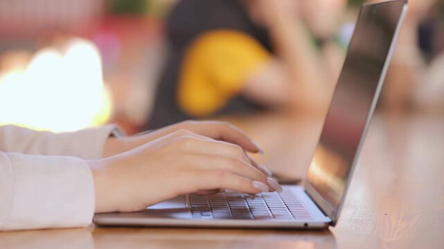 Woman is typing on a laptop. The laptop is open and the screen is black. The woman is wearing a white shirt