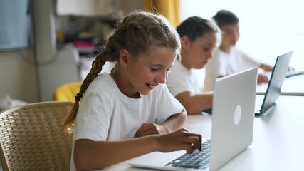 Girl using laptop and smiling in classroom with student and boy at table learning on computer while kid and child focus on screen during school study showing collaborative learning and education - Powered by Adobe
