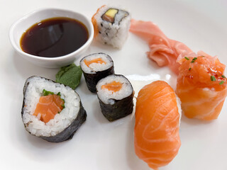 Sashimi and maki sushi on a white plate with a small bowl of soy sauce.