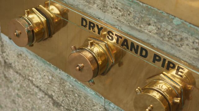 Closeup emergency standpipe coupling insitu inside concrete frame, fire safety trainer demonstrates attachment and function, warm metallic luster and functional hardware emphasized, training scenario