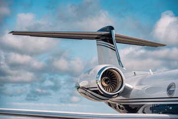 Close-up of a modern business jet tail and turbofan engine showing aerodynamic design and high-bypass fan blades under partly cloudy skies.