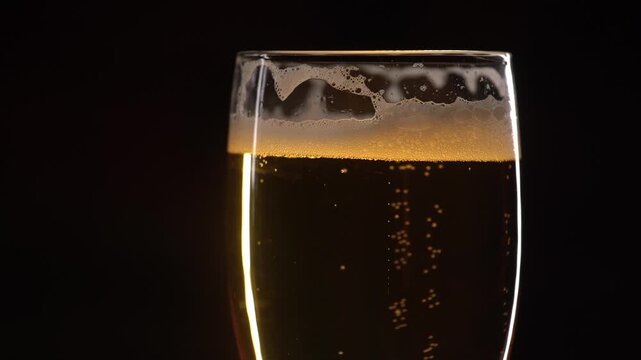 Fresh beer in a glass with bubbles on black background, close-up. Alcohol drink on a bar counter.
