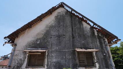 Old brick house with damaged and missing roof tiles, showing weathered exterior and vintage window design. Concept of building maintenance, urban decay, aging structure, and property inspection.