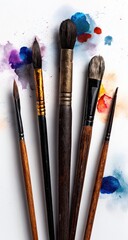 Assorted paintbrushes lie on a white surface with colorful watercolor splatters.