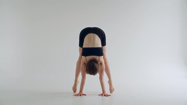 Young woman performing straddle handstand pose with legs wide apart and arms pressed into floor as practicing yoga in minimalist white studio