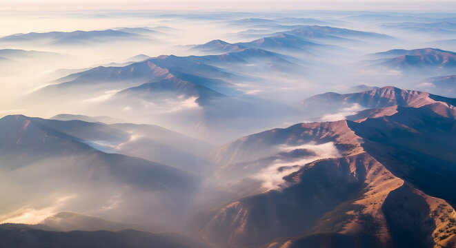 Aerial view of misty mountain range at sunrise with rugged terrain and soft fog