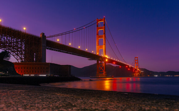 Golden Gate Bridge architectural landmark in San Francisco, California, USA, illuminated at night with reflections on the bay water, suspension bridge design, engineering structure, travel destination