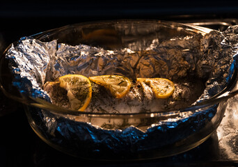 Baked in the oven in foil with spices, herbs and lemon in a baking dish, top view. Fresh baked walleye fish in foil for baking with vegetables, lemon and spices close-up. Pike-perch baked in foil. 