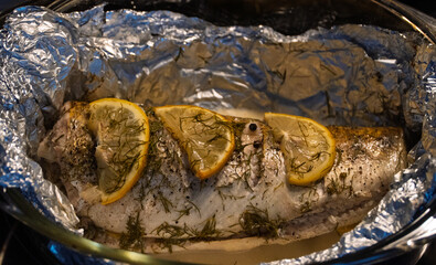 Baked in the oven in foil with spices, herbs and lemon in a baking dish, top view. Fresh baked walleye fish in foil for baking with vegetables, lemon and spices close-up. Pike-perch baked in foil. 