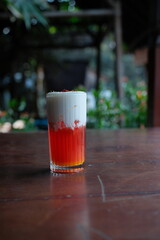 Refreshing red layered beverage with creamy foam top on rustic wooden table for a vibrant summer feel, perfect for food blogs and drink promotions