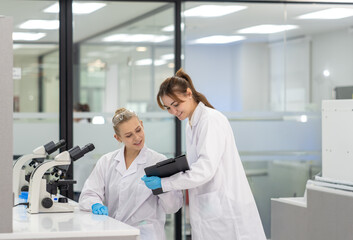 Obraz premium Two laboratory scientists collaborate on research while examining data on a tablet in a modern lab setting