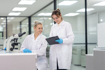 Two scientists discuss findings in a modern laboratory while one uses a microscope to conduct research