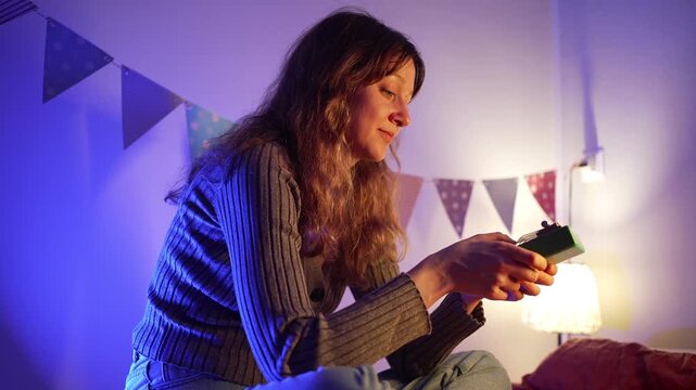 Cozy atmosphere in a room illuminated by colorful lights, where a young woman sits comfortably playing a kalimba, creating a peaceful and relaxing musical moment