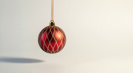 A single red Christmas bauble with a gold glitter pattern hanging on a ribbon. Minimalist holiday decoration on a plain background with copy space