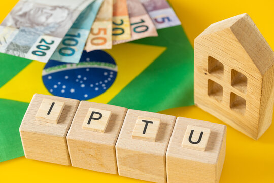  IPTU Brazil. An abbreviation for annual property tax. A financial and business concept. A symbol on wooden blocks, the Brazilian flag, a miniature house, and real banknotes