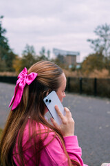 Young woman in pink talking on phone, side portrait outdoors