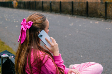 Young woman in pink talking on phone, side portrait outdoors