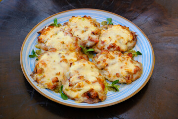 French-style meat delicious flavour meat chops layered with fried mushrooms, onion, tomato and covered with melted cheese in gratin dish on black stone slate tray, view from above. High quality photo