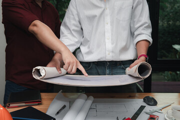Close-up of two architects discussing a blueprint on a desk. Concept of teamwork, architecture planning, engineering, and professional collaboration.
