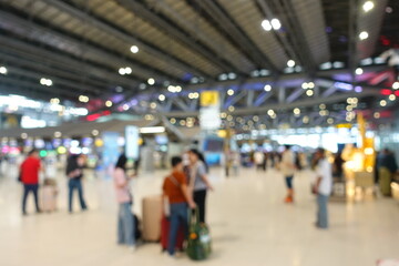 Blurred view of passengers and people at  International Airport. Travelers walking and checking flight information boards in the terminal. Busy atmosphere of people with luggage, lights, and airport.