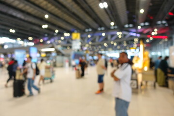 Blurred view of passengers and people at  International Airport. Travelers walking and checking flight information boards in the terminal. Busy atmosphere of people with luggage, lights, and airport.