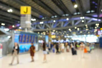 Blurred view of passengers and people at  International Airport. Travelers walking and checking flight information boards in the terminal. Busy atmosphere of people with luggage, lights, and airport.