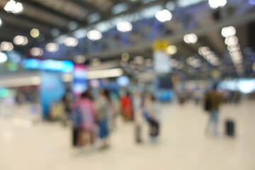 Blurred view of passengers and people at  International Airport. Travelers walking and checking flight information boards in the terminal. Busy atmosphere of people with luggage, lights, and airport.
