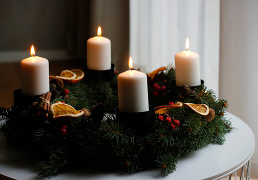 Handmade advent wreath with four burning white candles, spruce branches, dried orange slices, cinnamon sticks and red berries, creating a warm and cozy Christmas atmosphere on a winter table