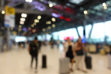 Blurred view of passengers and people at  International Airport. Travelers walking and checking flight information boards in the terminal. Busy atmosphere of people with luggage, lights, and airport.