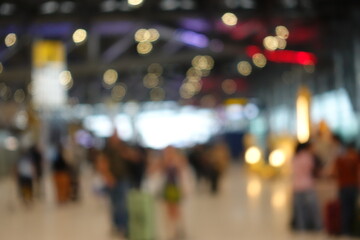 Blurred view of passengers and people at  International Airport. Travelers walking and checking flight information boards in the terminal. Busy atmosphere of people with luggage, lights, and airport.