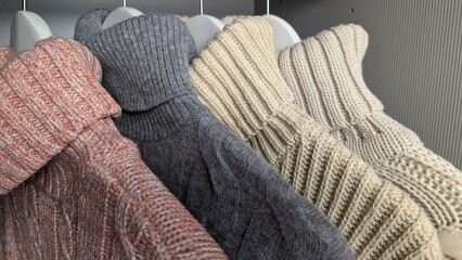 Close-up shot of sweaters in different colors hanging on wooden hangers in a wardrobe, 
