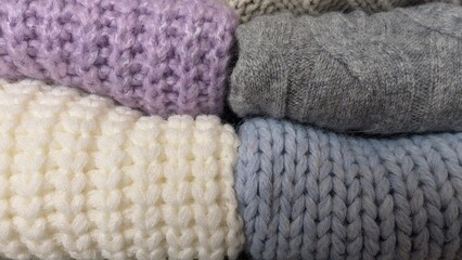 Stack of wool sweaters in different colors on a shelf, warm and cozy atmosphere.