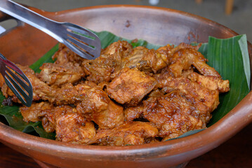 A close-up of Indonesian-style spicy chicken dish served in a traditional clay bowl lined with banana leaves